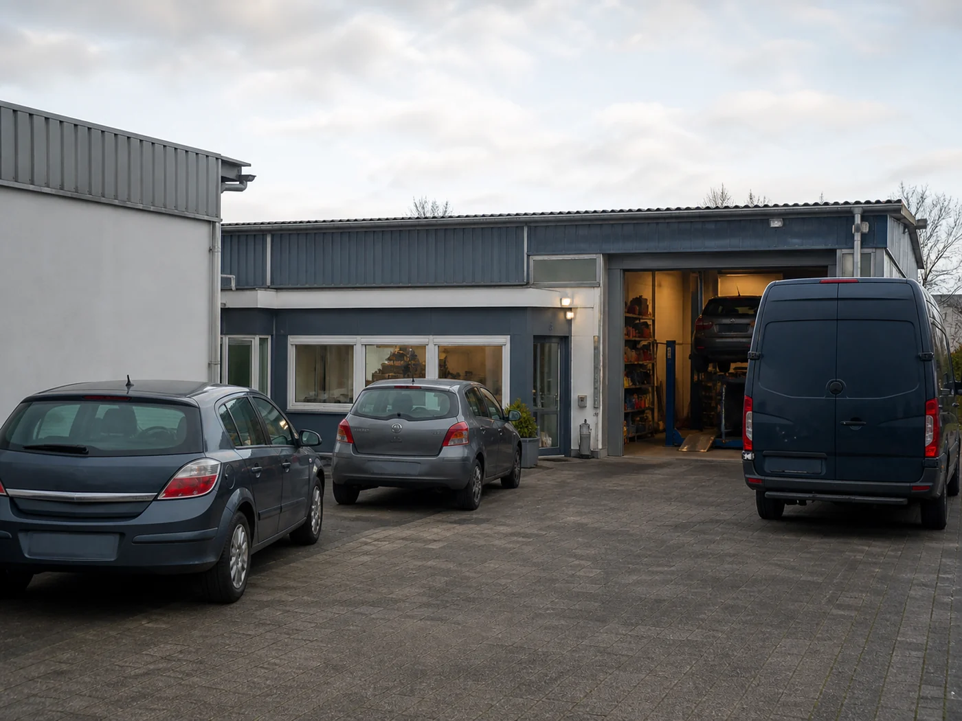 Der Hof einer Kfz-Werkstatt, Fahrzeuge vor dem offenen Hallentor